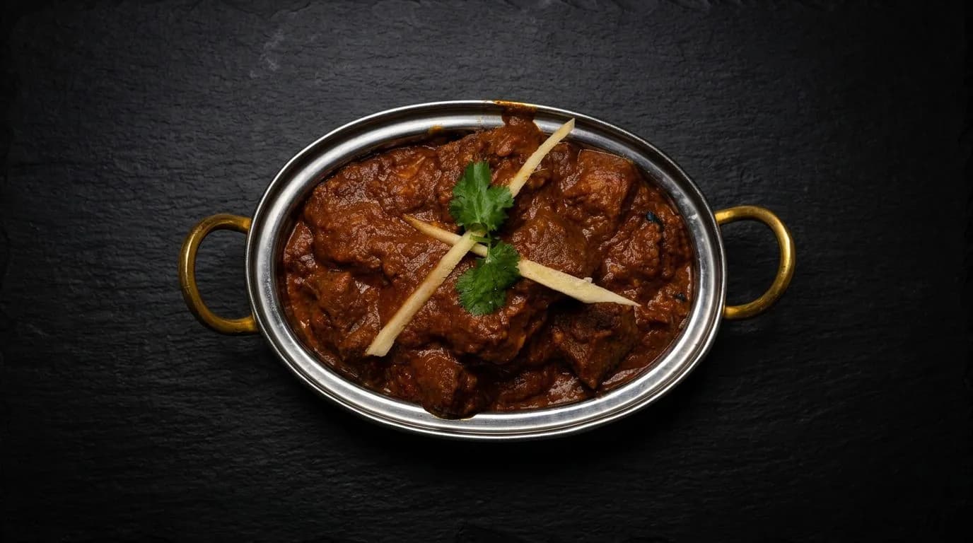 Lamb curry in a metal serving dish, garnished with ginger and coriander.